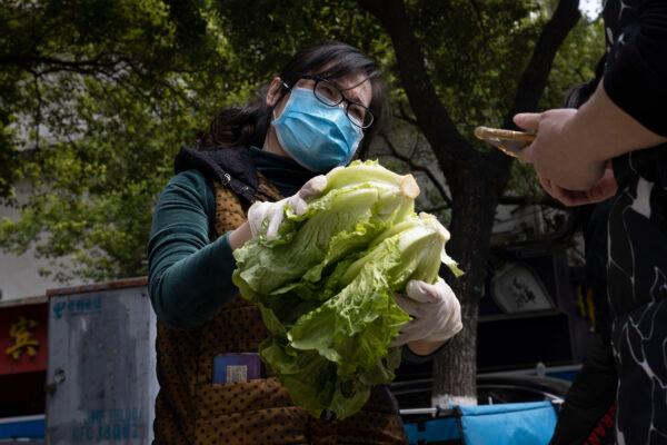 A resident volunteer hands over vegetables to a resident outside a community in Wuhan in central China's Hubei Province, China, on April 6, 2020. (Ng Han Guan/AP Photo)