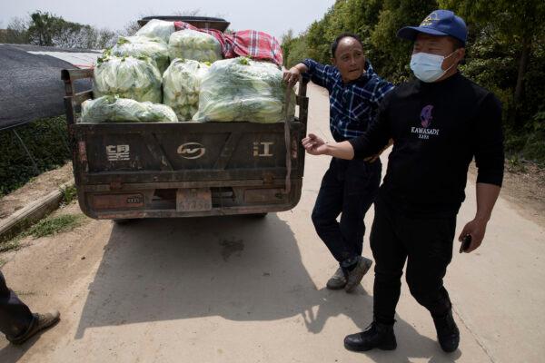 Volunteer Luo Hao (R) talks about his work near a farmer with his harvest of vegetable to be collected by other volunteers in Wuhan in central China's Hubei Province, China, on April 6, 2020. (Ng Han Guan/AP Photo)
