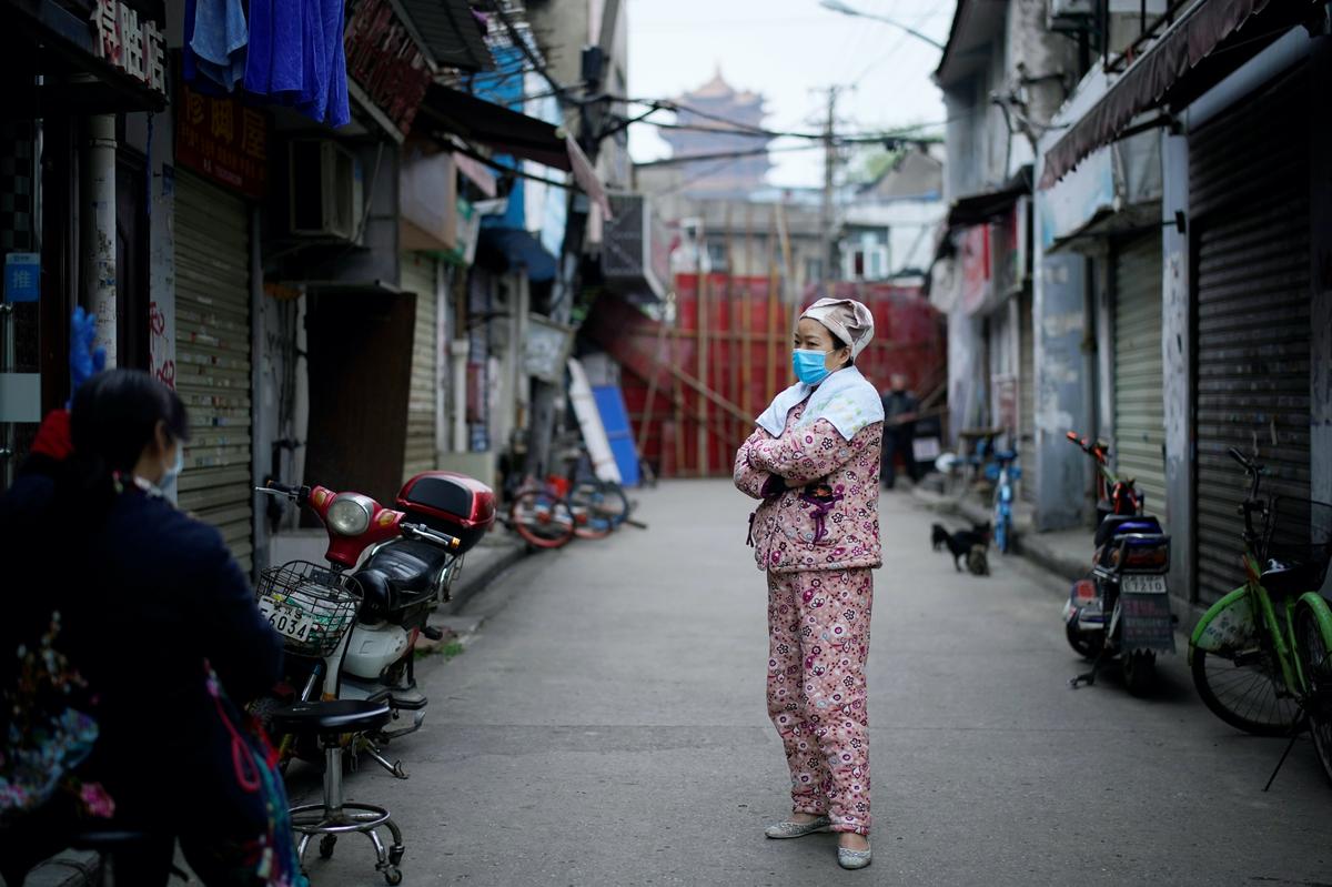 A resident wears a protective mask as she stands near an old residential community blocked by barriers in CCP virus epicenter Wuhan, China, on April 5, 2020. (Reuters/Aly Song)