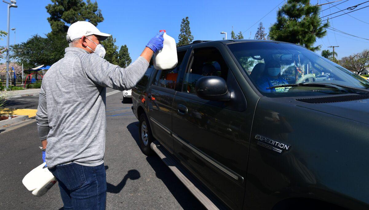 A gallon of milk is offered as volunteers help distribute food as vehicles arrive at a Los Angeles Regional Food Bank drive-through giveaway in Pico Rivera, California, on April 28, 2020. (Frederic J. Brown/AFP via Getty Images)