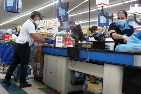 Lay Guzman stands behind a partial protective plastic screen and wears a mask and gloves as she works as a cashier at the Presidente Supermarket in Miami, Fla., on April 13, 2020. (Joe Raedle/Getty Images)