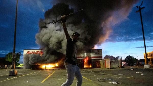 A man poses for a photo in the parking lot of an AutoZone store in flames, while protesters hold a rally for George Floyd in Minneapolis on May 27, 2020. (Carlos Gonzalez/Star Tribune via AP)