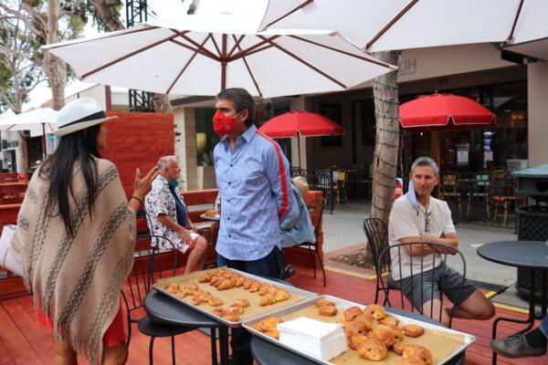 Laurent Vrignaud (C) serves pastries to pedestrians in the newly opened promenade in Laguna Beach, Calif., on June 15, 2020. (Jamie Joseph/The Epoch Times)