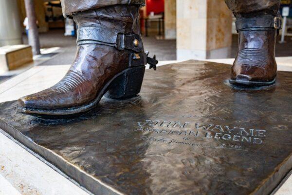 The words "John Wayne American Legend" are engraved on the platform below a statue of the actor at the John Wayne Airport in Orange County, Calif. (John Fredricks/The Epoch Times)