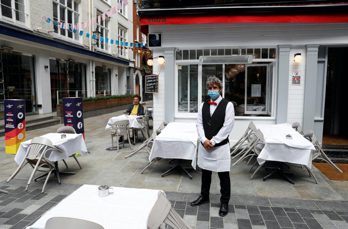 A waiter poses for photographs as he waits for customers outside a restaurant, after it reopened following the COVID-19 outbreak, in London, UK, on July 5, 2020. (Peter Nicholls/Reuters)