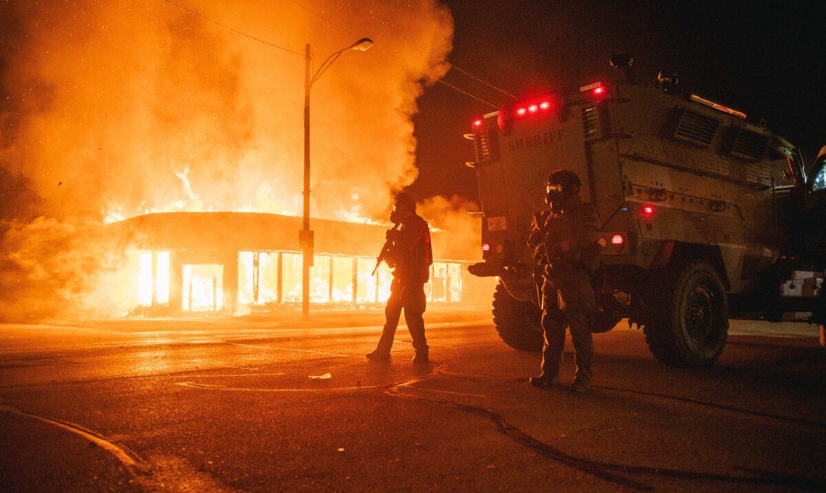 A police armored vehicle patrols an intersection while a building set afire by rioters burns in Kenosha, Wis., on Aug. 24, 2020. (Brandon Bell/Getty Images)