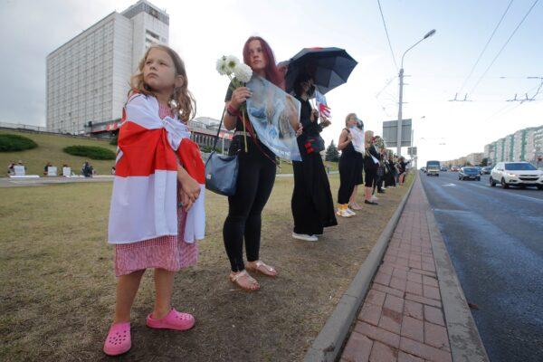A girl covers with an old Belarusian National flag as people stand near the place where Alexander Taraikovsky died amid the clashes protesting the election results, in Minsk, on Aug. 24, 2020. (Dmitri Lovetsky/AP Photo)