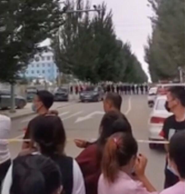In this image made from video taken in August 2020, parents gather behind a police line outside a school in Tongliao in Northwestern China's Inner Mongolia region. (AP Photo)