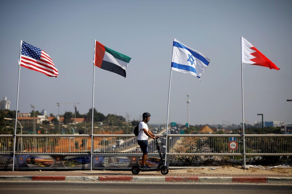 A man rides a scooter near the flags of the United States, the United Arab Emirates, Israel, and Bahrain as they flutter along a road in Netanya, Israel on Sept. 14, 2020. (Nir Elias/Reuters)