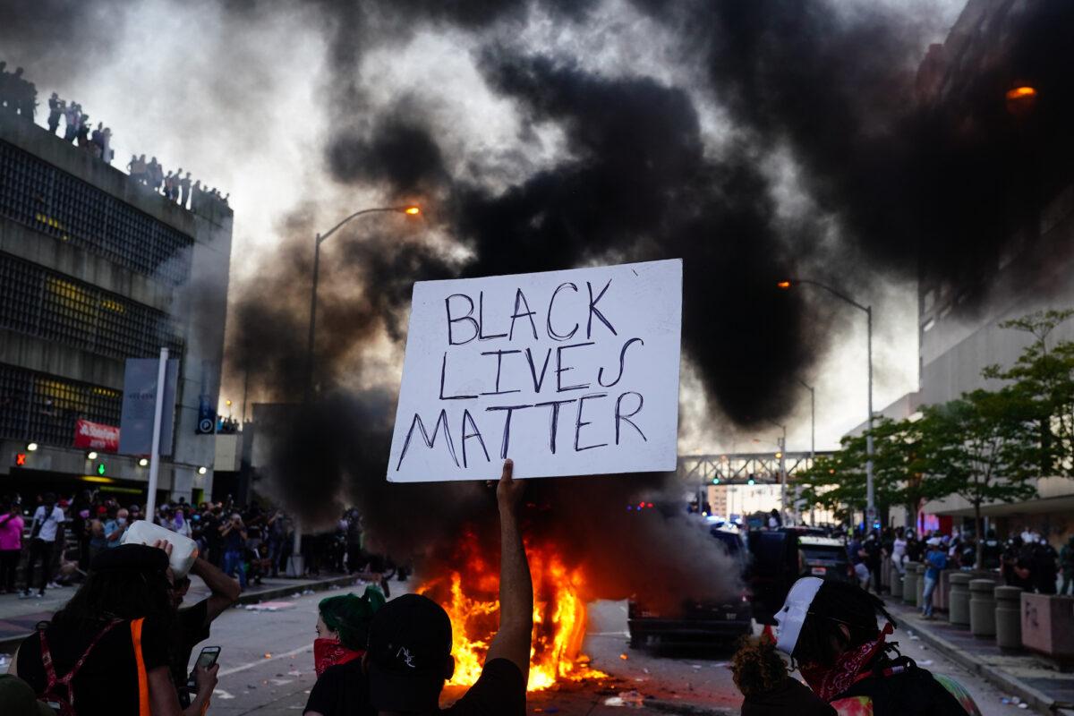 A man holds a Black Lives Matter sign as a police car burns in front of him during a protest outside CNN Center in Atlanta on May 29, 2020. (Elijah Nouvelage/Getty Images)