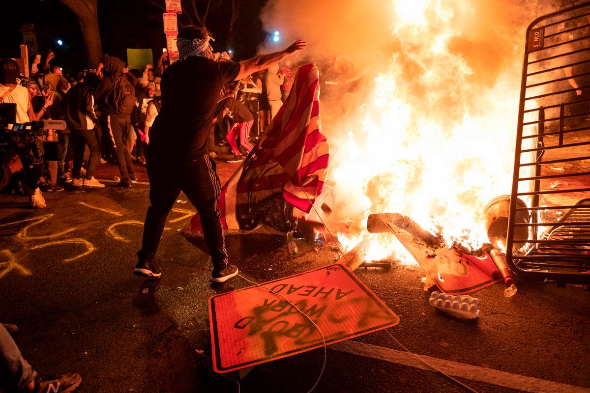A protester throws a U.S. flag into a burning barricade during a demonstration against the death of George Floyd near the White House on May 31, 2020, in Washington. (ROBERTO SCHMIDT/AFP via Getty Images)