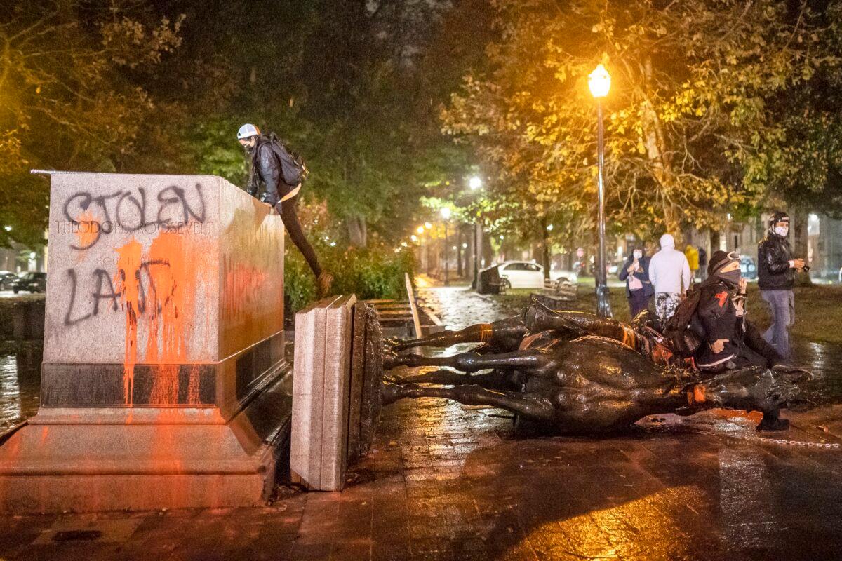 People stand near the toppled statue of President Theodore Roosevelt during a riot in Portland, Ore., on Oct. 11, 2020. (Nathan Howard/Getty Images)