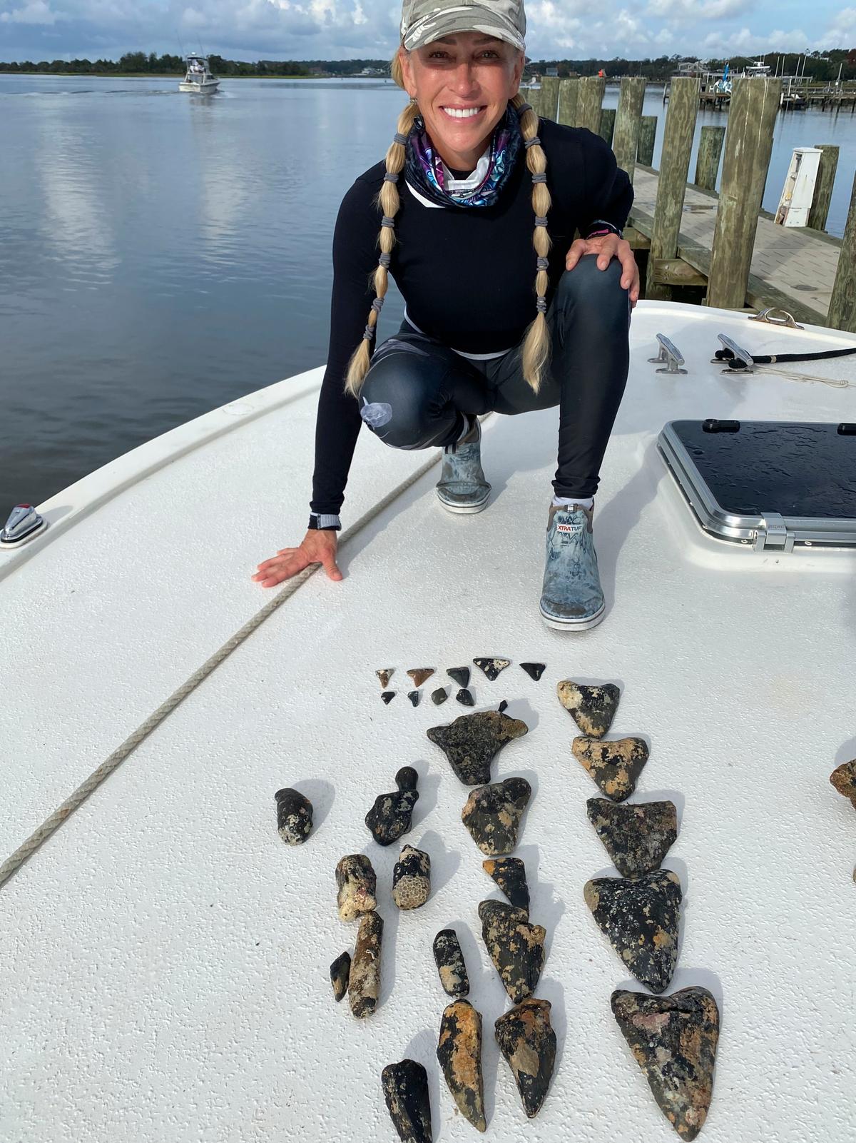 Terri Olah, 53, with some of the teeth she found on a recent dive. The megalodon teeth are on the far right. (Caters News)