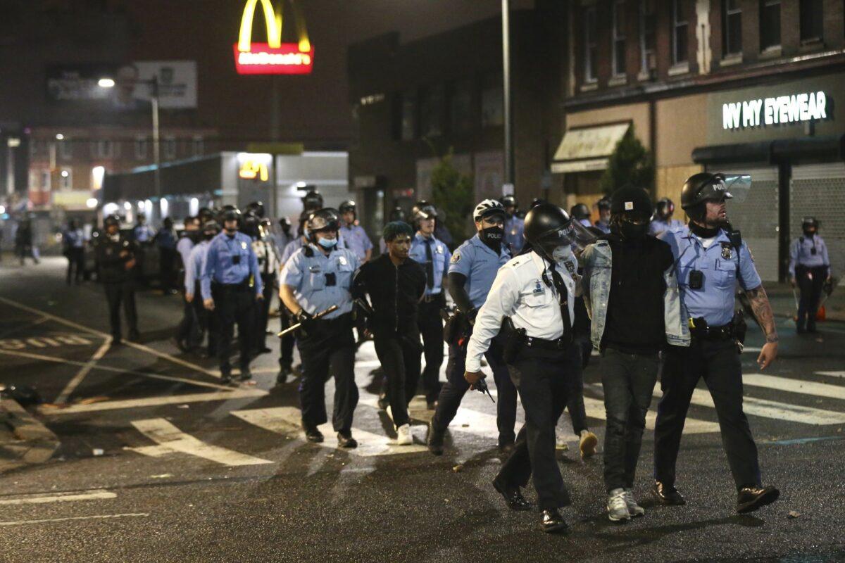 Police lead several people in handcuffs to a police van on 52nd Street in West Philadelphia in the early hours of Oct. 27, 2020. (Tim Tai/The Philadelphia Inquirer via AP)