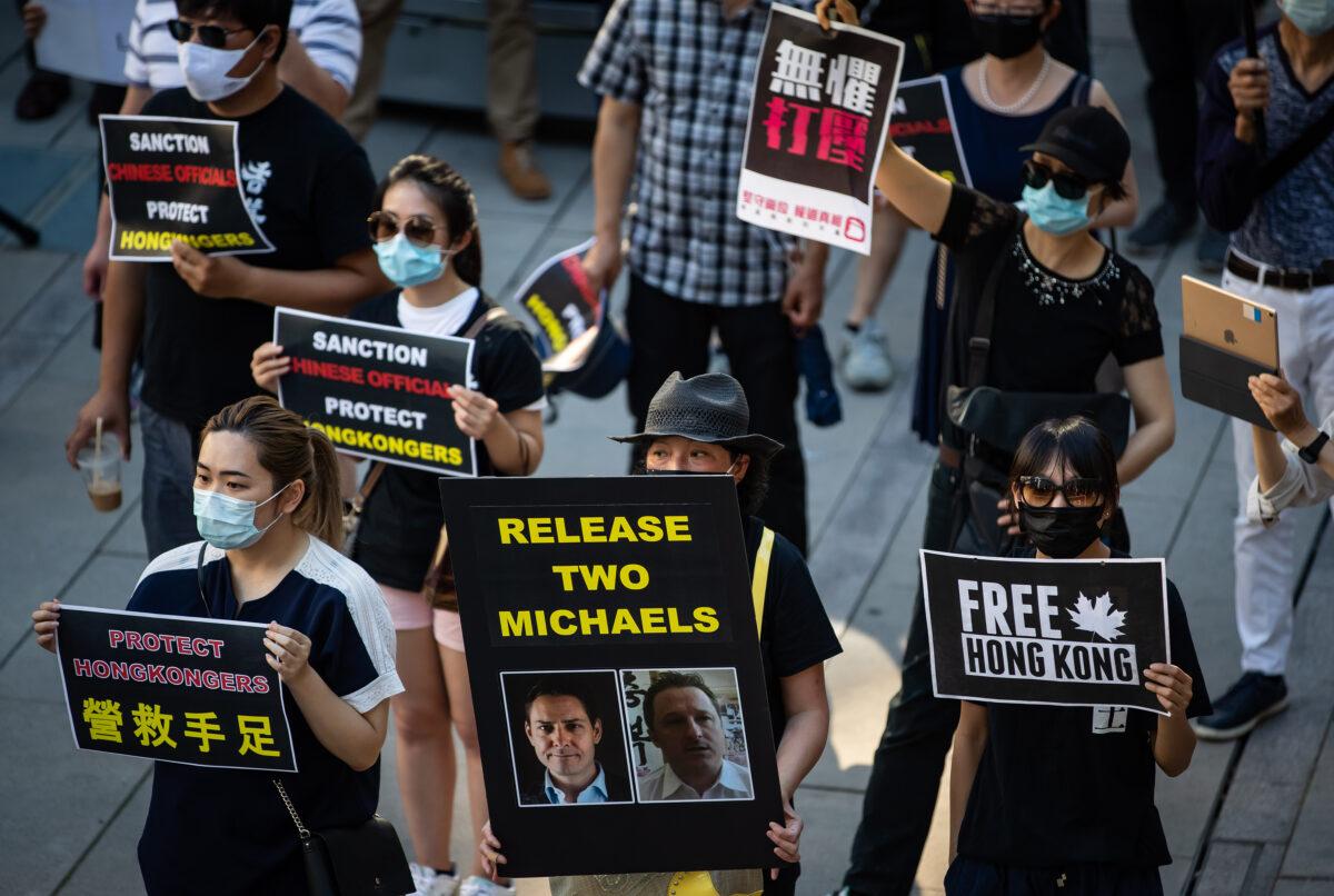 A woman holds a sign with photographs of Michael Kovrig and Michael Spavor, who have been detained in China since December 2018, during a rally in support of Hong Kong democracy in Vancouver, B.C., Canada, on Aug. 16, 2020. (Darryl Dyck/The Canadian Press)