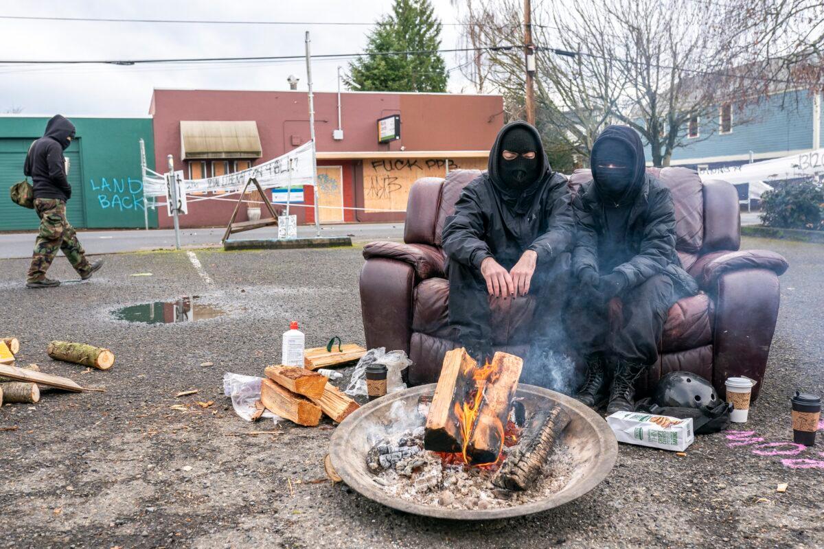 Two protesters in black sit near a fire inside an eviction blockade in Portland, Ore., on Dec. 10, 2020. (Nathan Howard/Getty Images)