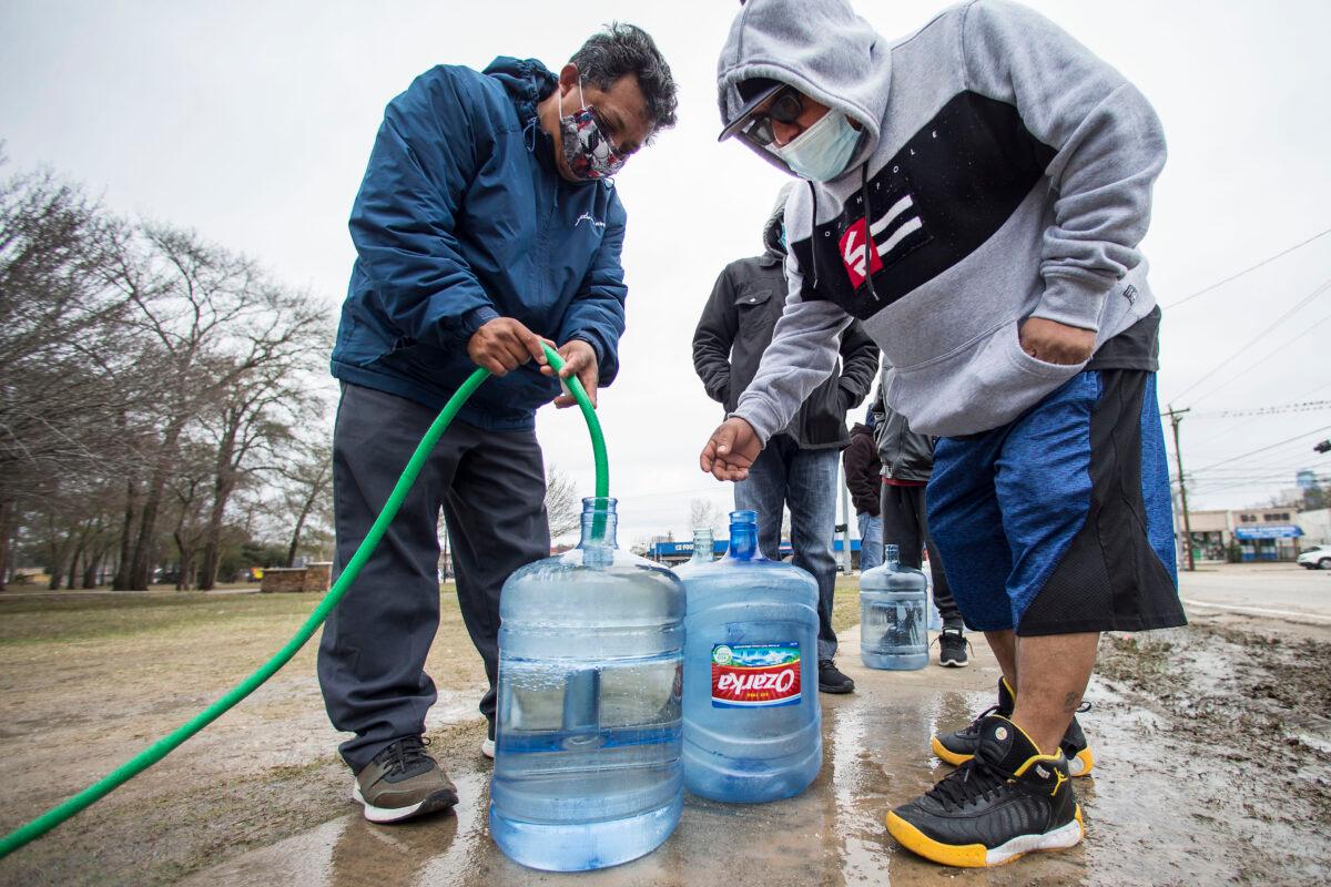 Victor Hernandez (L) and Luis Martinez fill their water containers with a hose from a spigot in Haden Park, in Houston, Texas, on Feb. 18, 2021. (Brett Coomer/Houston Chronicle via AP)
