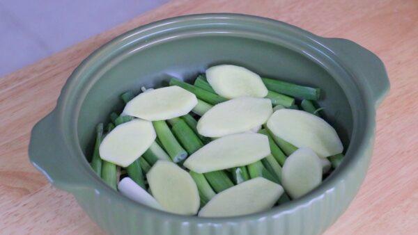 Line the bottom of the clay pot with scallions and ginger. (CiCi Li)