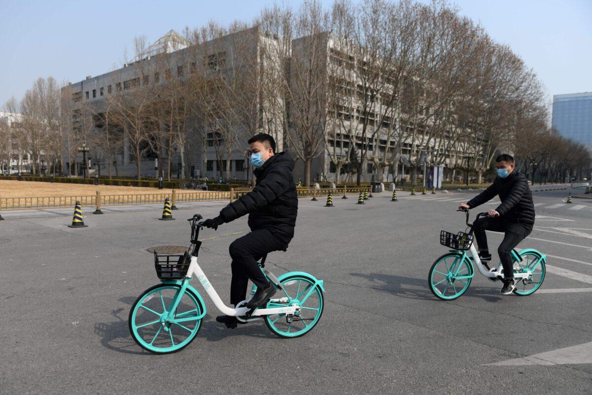 Two men ride bikes on the empty grounds of Tsinghua University in Beijing on Feb. 28, 2020. (Greg Baker/AFP via Getty Images)