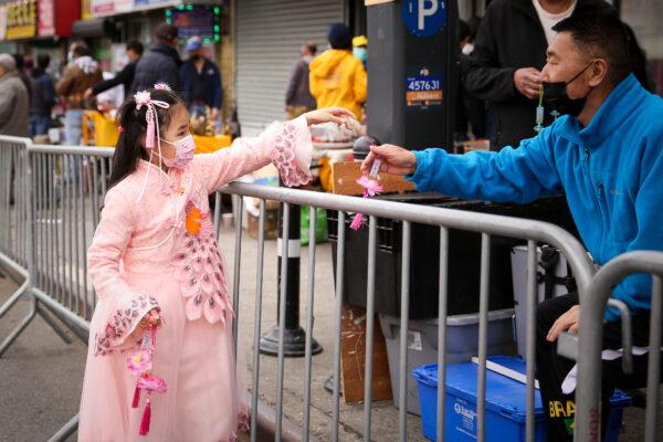 A young Falun Gong practitioner hands out lotus flowers at a parade in Flushing, New York, on April 18, 2021, to commemorate the 22nd anniversary of the April 25th peaceful appeal of 10,000 Falun Gong practitioners in Beijing. (Samira Bouaou/The Epoch Times)