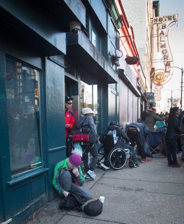A woman sits on the ground after injecting herself with an unknown substance outside Insite, the supervised injection site, in the Downtown Eastside of Vancouver, B.C., on Feb. 21, 2017. (The Canadian Press/Darryl Dyck)