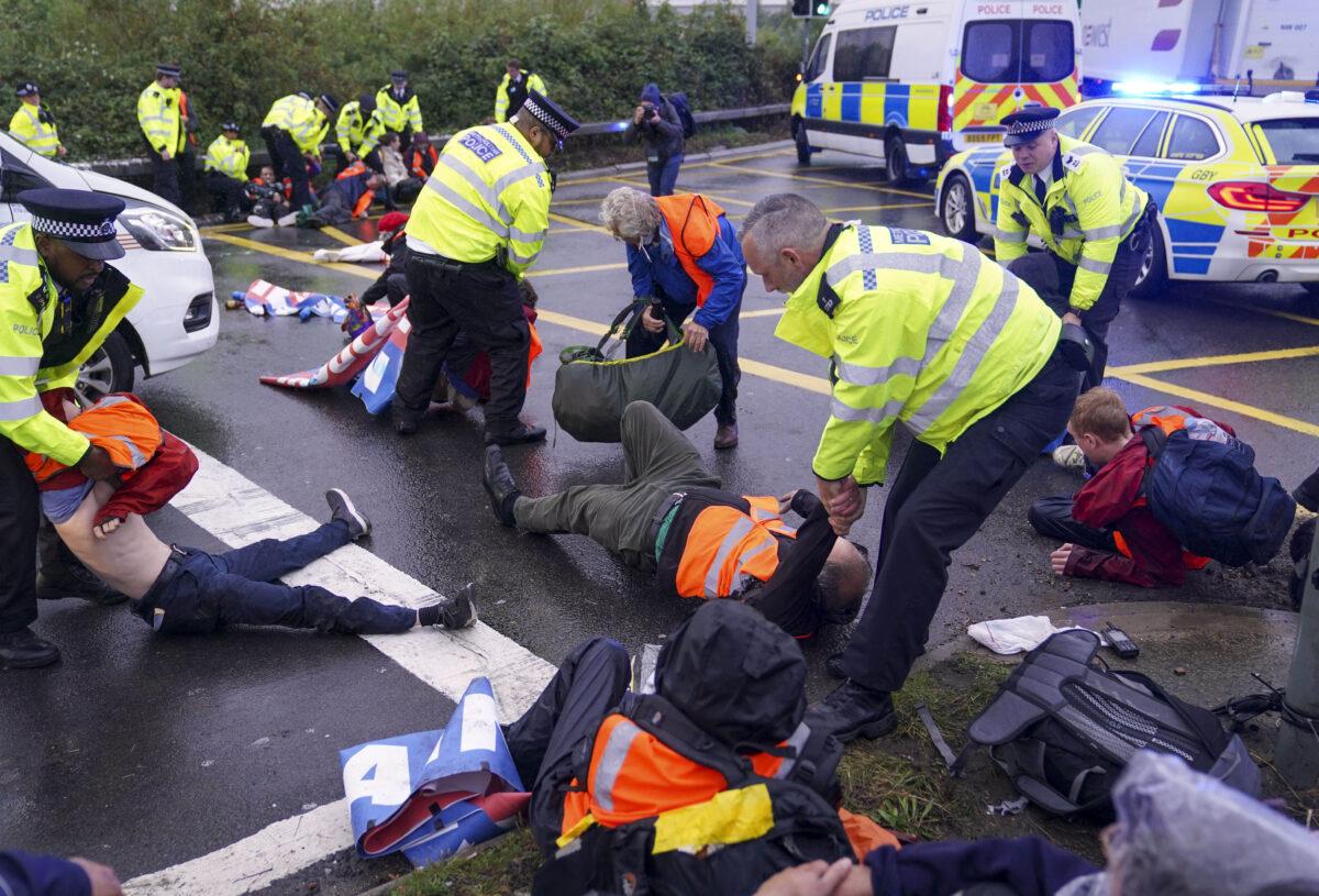 Police officers detain a protester from Insulate Britain occupying a roundabout leading from the M25 motorway to Heathrow Airport in London on Sept. 27, 2021. (Steve Parsons/PA)
