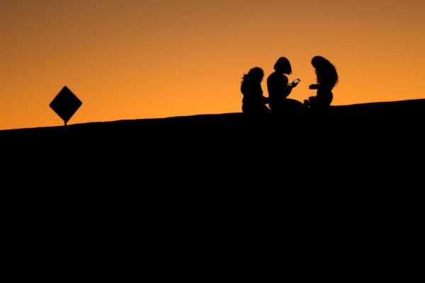 Young girls look at their phones as they sit on a hillside after sunset in El Paso, Texas, on June 20, 2018. (Mike Blake/Reuters)