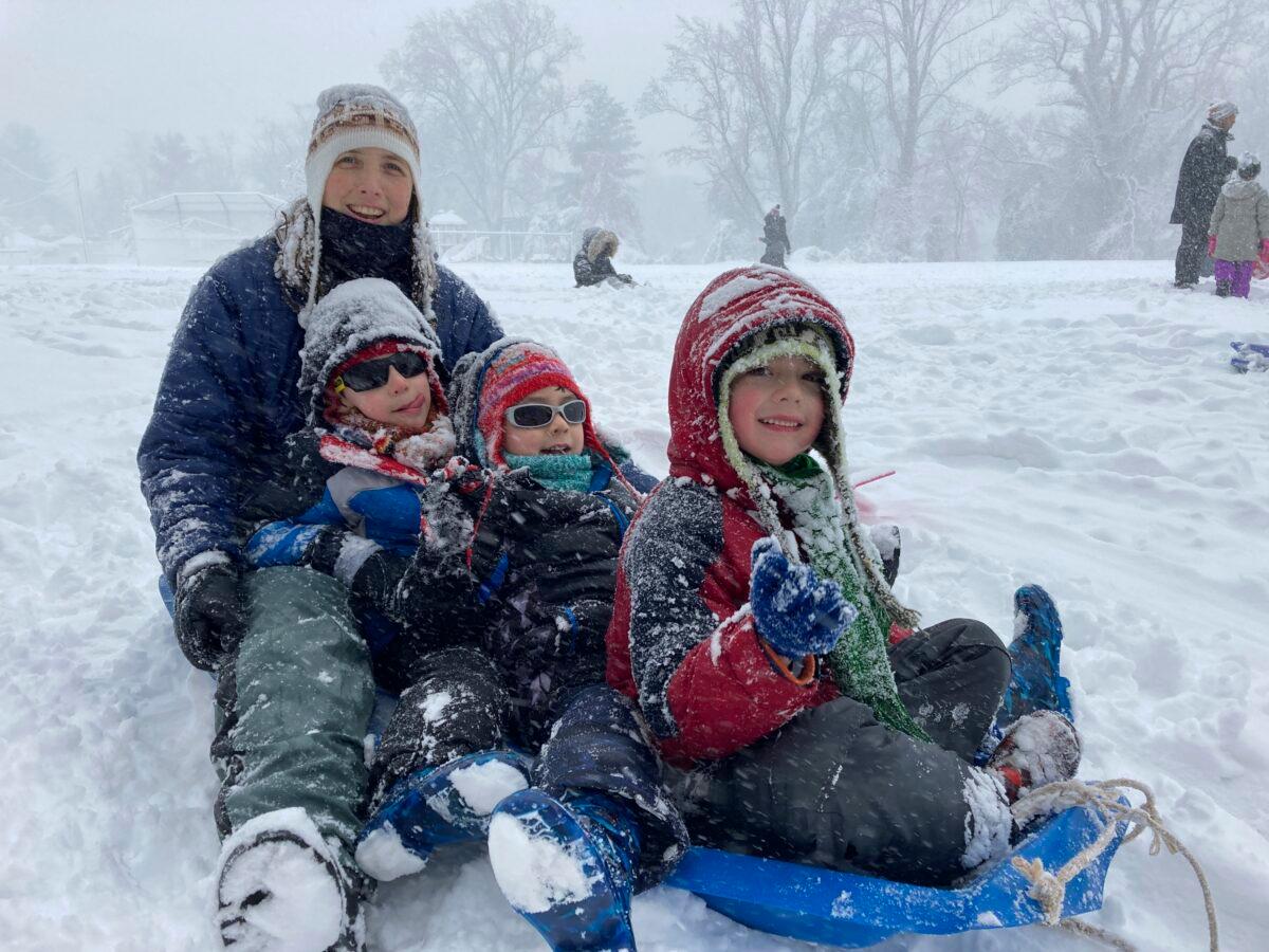 Lily Whitesell and her three children—Silvio, Thiago, and Inti Carvallo—prepare to descend the big hill behind Lemon Road Elementary during a snow storm in Falls Church, Va., on Jan. 3, 2022. (Matthew Barakat/AP Photo)