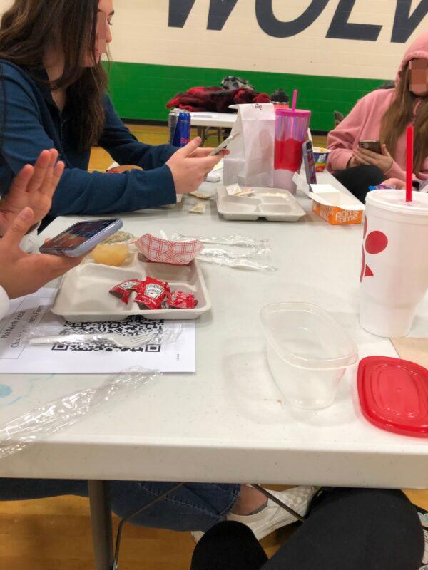 Unmasked students taking lunch in the auxiliary gym at Woodgrove High School in Purcellville, Va., from Jan. 25 to Jan. 28, 2022. A “no mask area” check-in sheet with a QR code is on the table. (Courtesy of Erin Dunbar)