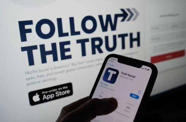 A person checks the app store on a smartphone for "Truth Social"—owned by Trump Media & Technology Group—with its website on a computer screen in the background, in Los Angeles, Oct. 20, 2021. (Chris Delmas/AFP via Getty Images)