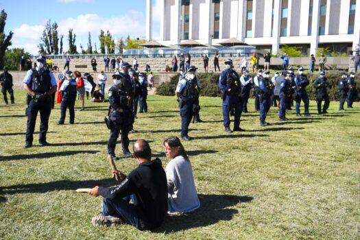Protesters sit as police officers remove camping equipment at makeshift camp next to the National Library in Canberra, Australia, on Feb. 4, 2022. A camp of protesters in Canberra has been given a move on order by police. (AAP Image/Lukas Coch)