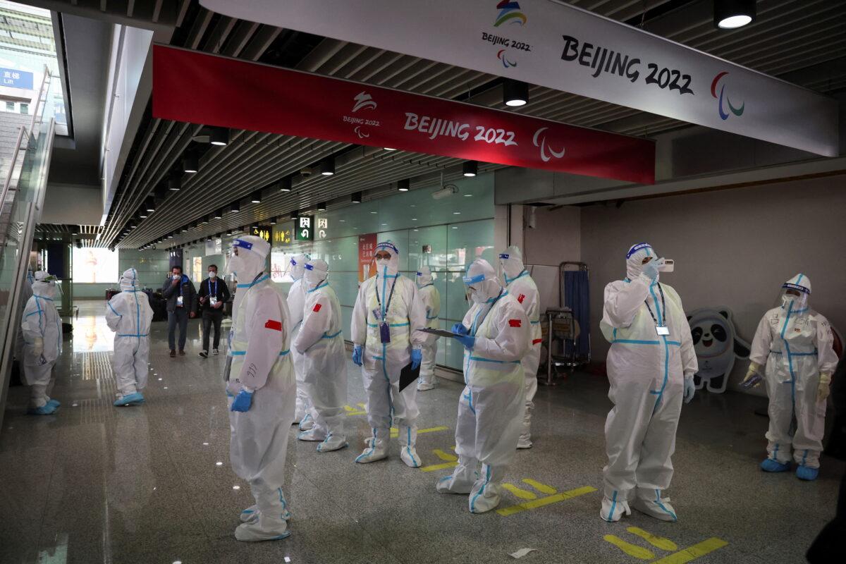 People wearing personal protective equipment, designed to prevent the spread of COVID-19, stand inside Beijing Capital International Airport ahead of the Beijing 2022 Winter Olympics on Jan. 31, 2022. (Phil Noble/Reuters)