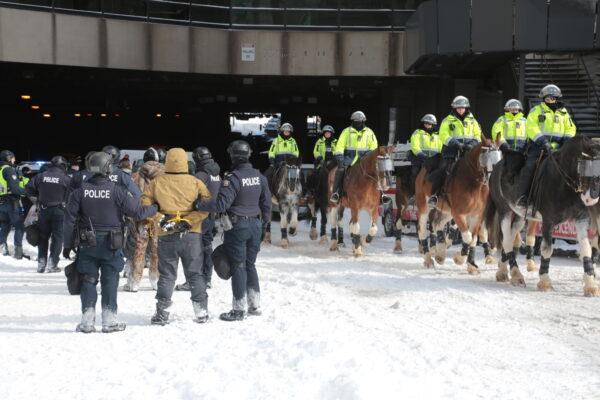 Police hold several arrested people as mounted officers move towards the main protest on Feb. 18, 2022. (Richard Moore/The Epoch Times)