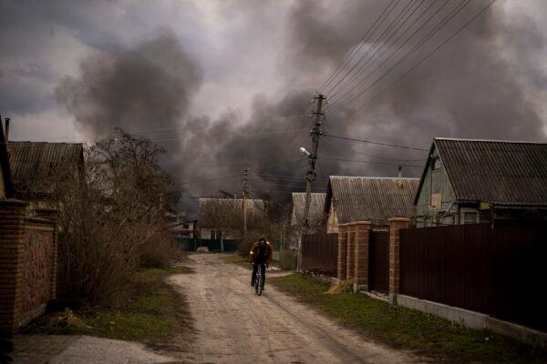 A Ukrainian man rides his bicycle near a factory and a store burning after it was bombarded in Irpin, on the outskirts of Kyiv, Ukraine, on March 6, 2022. (Emilio Morenatti/AP Photo)