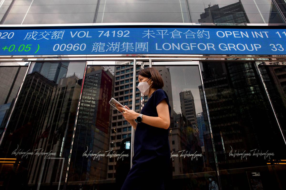 A woman walks past a digital sign showing stock market information in the Central district of Hong Kong on Nov. 5, 2021. (Isaac Lawrence/AFP via Getty Images)