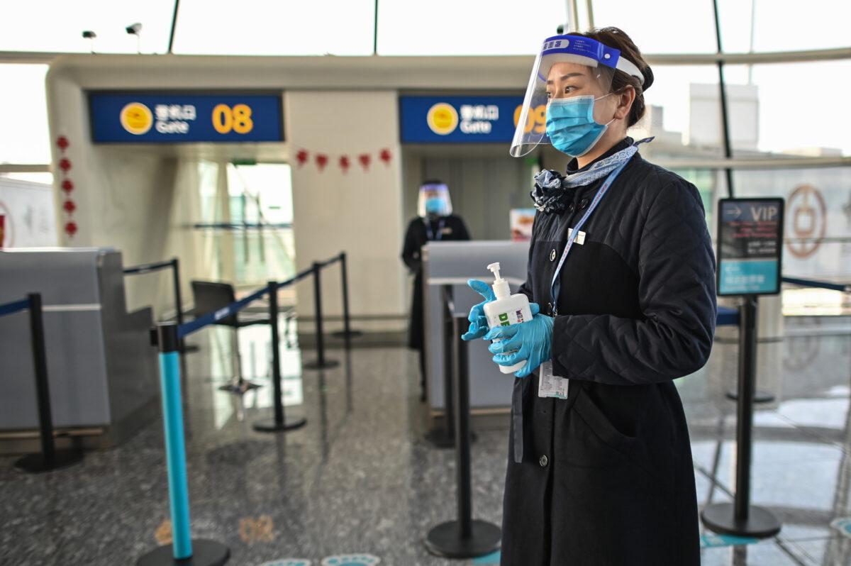 An airline worker wearing a safety mask and shield as a preventive measure against the COVID-19 coronavirus waits with alcohol gel for passengers to sanitize their hands at Tianhe International Airport in Wuhan, on Feb. 12, 2021. (Hector Retamal/AFP via Getty Images)