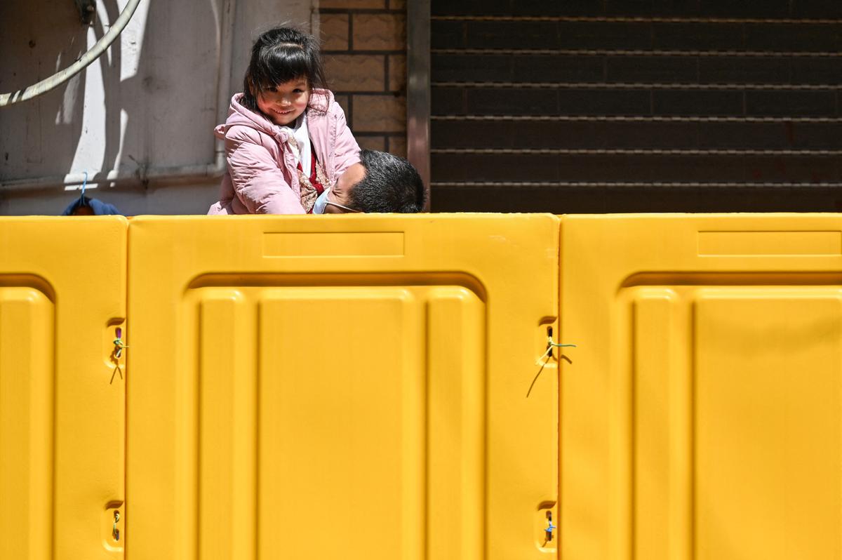 A father holds his daughter behind barriers that separate a neighborhood in lockdown as a measure against COVID-19 in Jing'an district in Shanghai on March 29, 2022. (Hector Retamal/AFP via Getty Images)