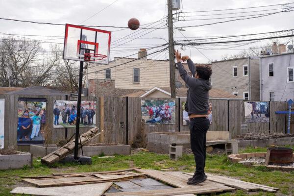 Hugo Limon Jr. plays basketball on a mini court inside a community garden on his block in the West Humboldt Park neighborhood of Chicago on April 11, 2022. The garden turns muddy after it rains, and he covers the ground with planks before playing. (Cara Ding/The Epoch Times)