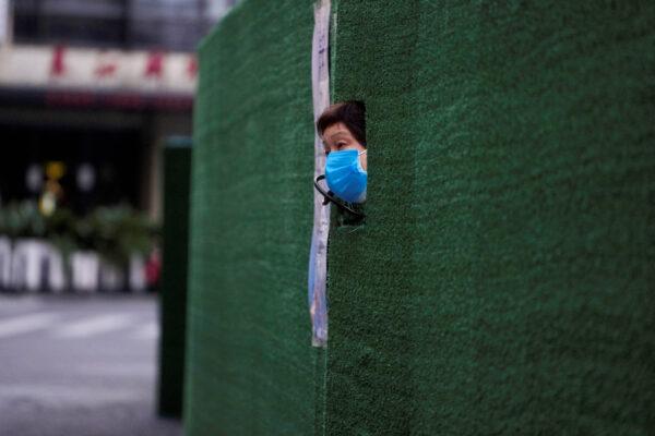A woman looks out through a gap in the barrier in a residential area in lockdown because of the COVID-19 pandemic, in Shanghai, China, May 6, 2022. (Aly Song/Reuters)