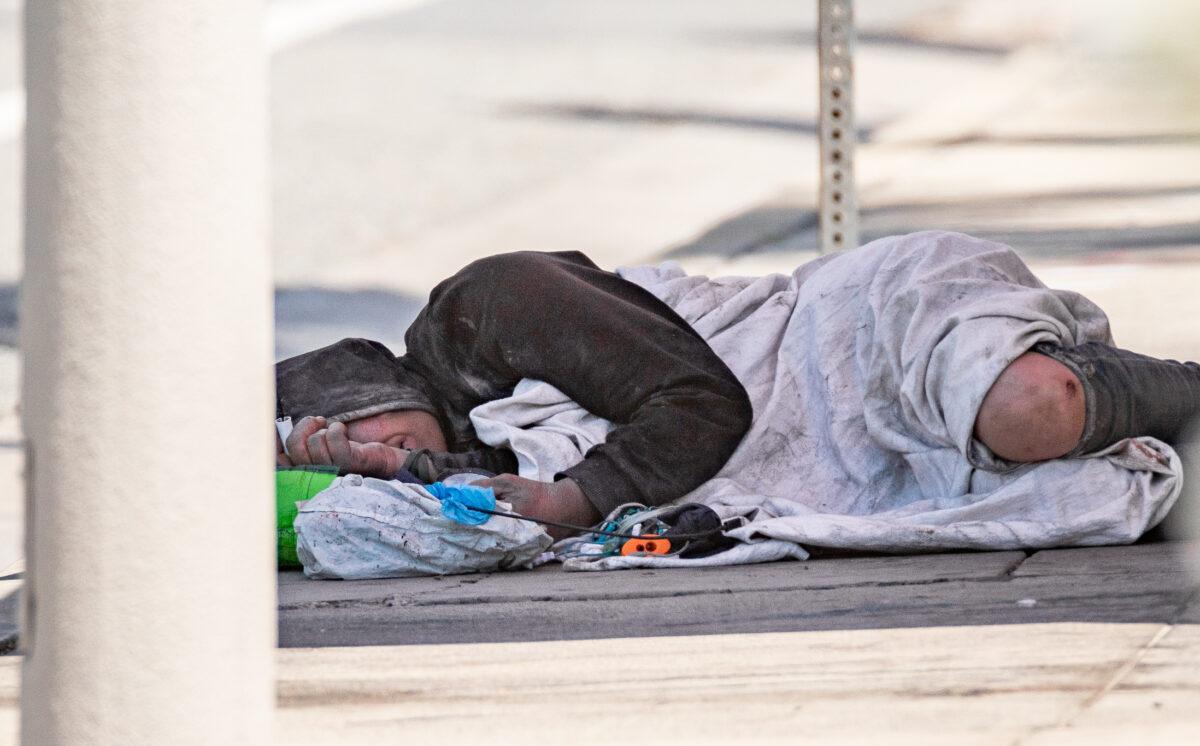 A homeless man sleeps in the shade of a bus stop in Santa Ana, Calif., on May 10, 2022. (John Fredricks/The Epoch Times)