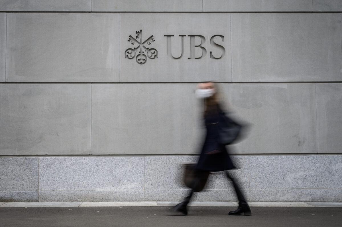 A pedestrian wearing a face mask to protect against Covid-19 walks by the logo of Swiss banking giant UBS engraved on the wall of its headquarters in Zurich on March 3, 2021. (Fabrice Coffrini/AFP via Getty Images)