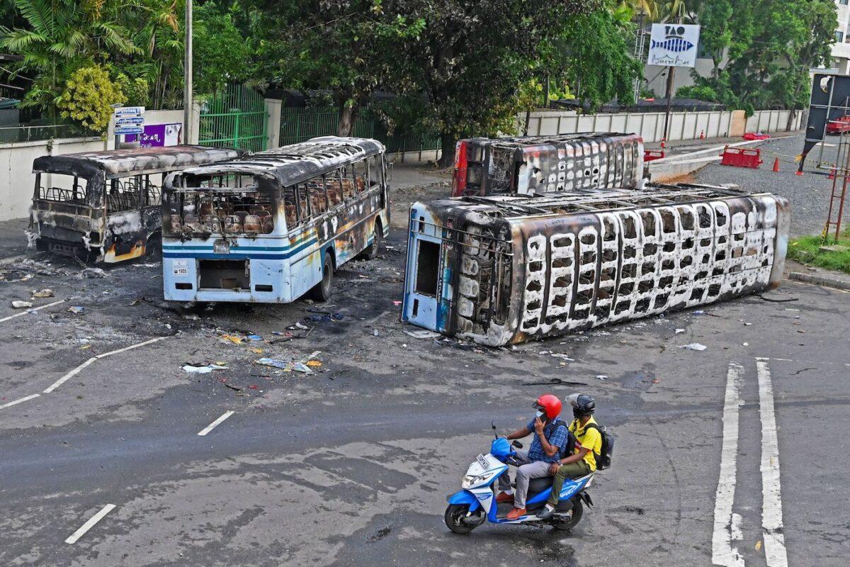 Men on a scooter ride past the burnt buses near Sri Lanka's former prime minister Mahinda Rajapaksa's official residence "Temple Trees," a day after they were torched by protesters in Colombo on May 10, 2022. (Ishara S. Kodikara/AFP via Getty Images)
