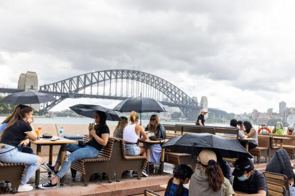 Patrons of the Opera Bar shelter under umbrellas during a rain shower in Sydney, Australia, on Dec. 29, 2021. (Jenny Evans/Getty Images)