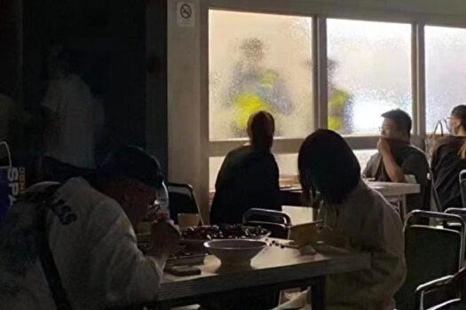 A restaurant in Shanghai with customers and two guards standing outside a window that has privacy glass in June 2022. (Screenshot via The Epoch Times)