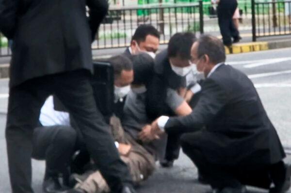 A man, center, is detained near the site of gunshots in Nara, western Japan, on July 8, 2022. (Kyodo News via AP)