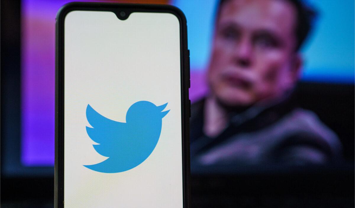 The Twitter logo is seen on a smartphone with Elon Musk in the background. (Rokas Tenys/Shuttertock)