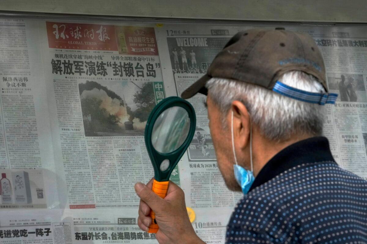 A man uses a magnifying glass to read a newspaper headline reporting the Chinese People's Liberation Army (PLA) conducting military exercises at a stand in Beijing on Aug. 7, 2022. (Andy Wong/AP Photo)