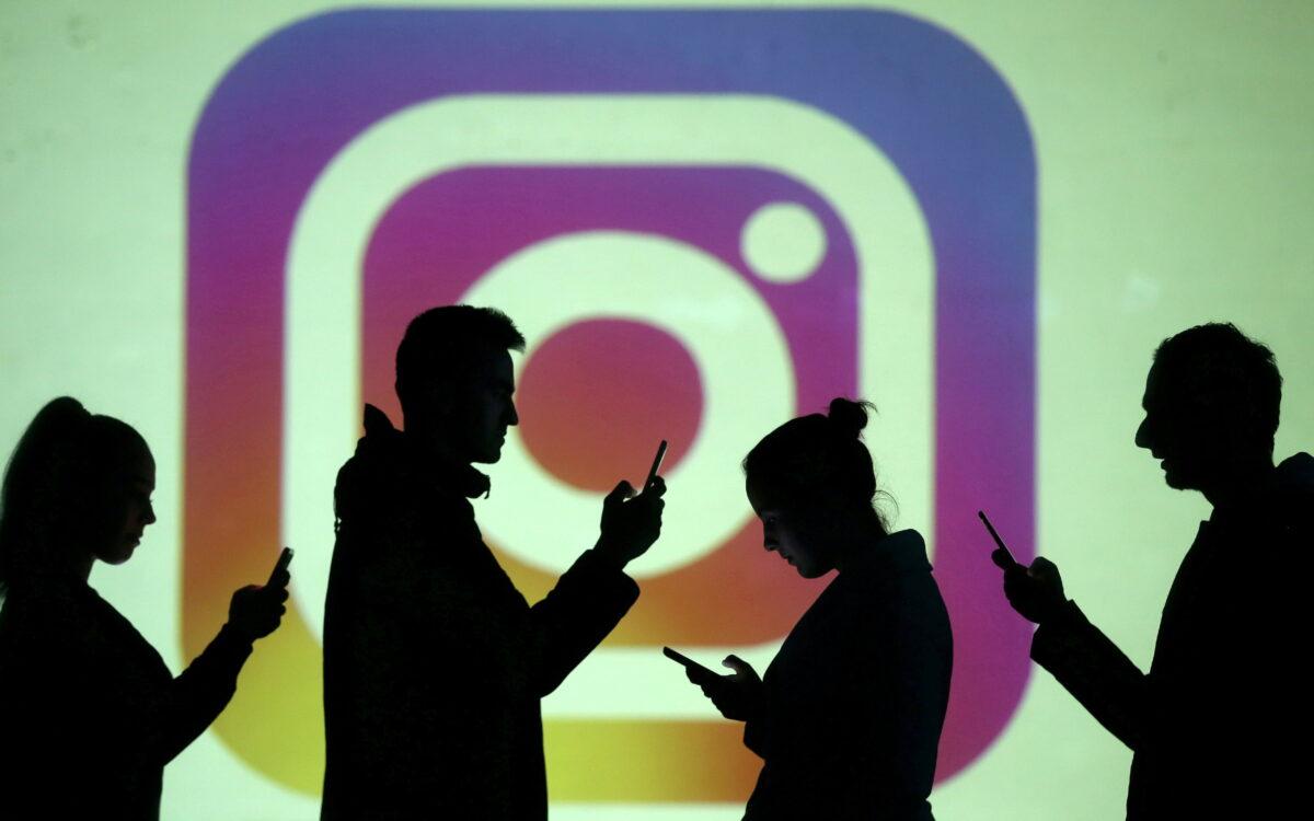 Silhouettes of mobile users are seen next to a screen projection of the Instagram logo, on March 28, 2018. (Dado Ruvic/Reuters)