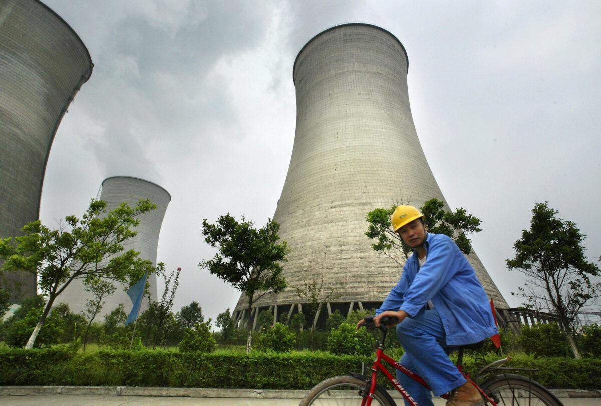 A worker rides past coal-fueled cooling towers at a power plant in Guangan, in southwest China's Sichuan province, on Aug. 22, 2004. (Frederic Brown/AFP via Getty Images)