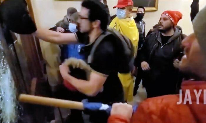 Christopher Grider (draped in yellow flag) watches as Zachary Alam smashes windows at the Speaker's Lobby entry on Jan. 6, 2021. (JaydenX/Screenshot via The Epoch Times)
